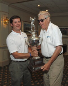 Pat Browne III and Pat Browne Jr. hold the Corcoran Cup trophy together at the Guiding Eyes annual golf event.