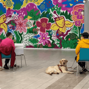 two students and their guides sit near colorful mural