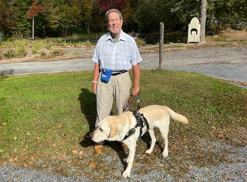 Jeffrey stands outside in his yard with yellow Lab guide dog Armstrong in harness