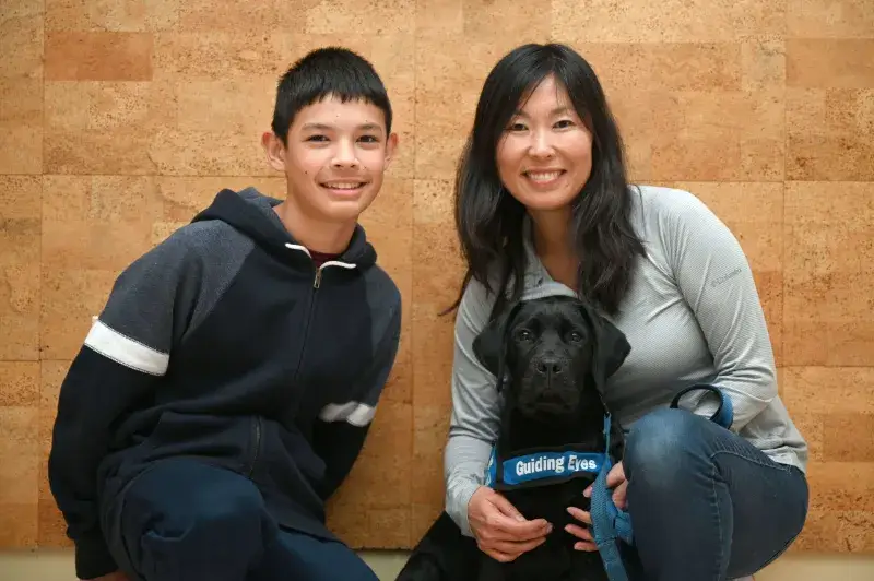 Two puppy raisers pose with a black lab during class