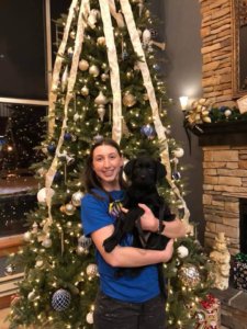 Julia holds black lab puppy Dakota in front of a beautifully decorated Christmas tree.