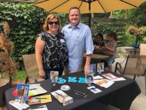 Renee and her husband pose for a photo with a table set up to promote Guiding Eyes during a street fair.