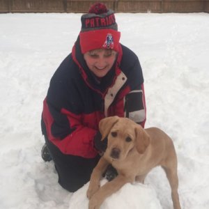 Kari kneels in the snow next to Yetta, a yellow lab pictured during her puppy days.