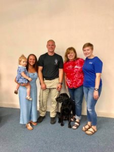 Renee and her daughter pose for a photo with black lab Yogi after his graduation from the Connecticut State Police detection program. The pair are joined by Yogi's new handler and his family.