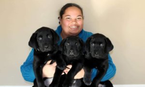 MeKalea smiles as she holds three black lab puppies in her arms.