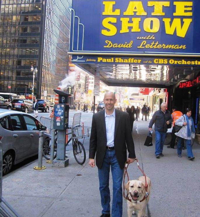 Tom Panek and Guiding Eyes Gus smile in front of the Late Show studio in NYC