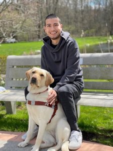 Graduate Arturo sits on a bench with guide dog Vangie at his feet