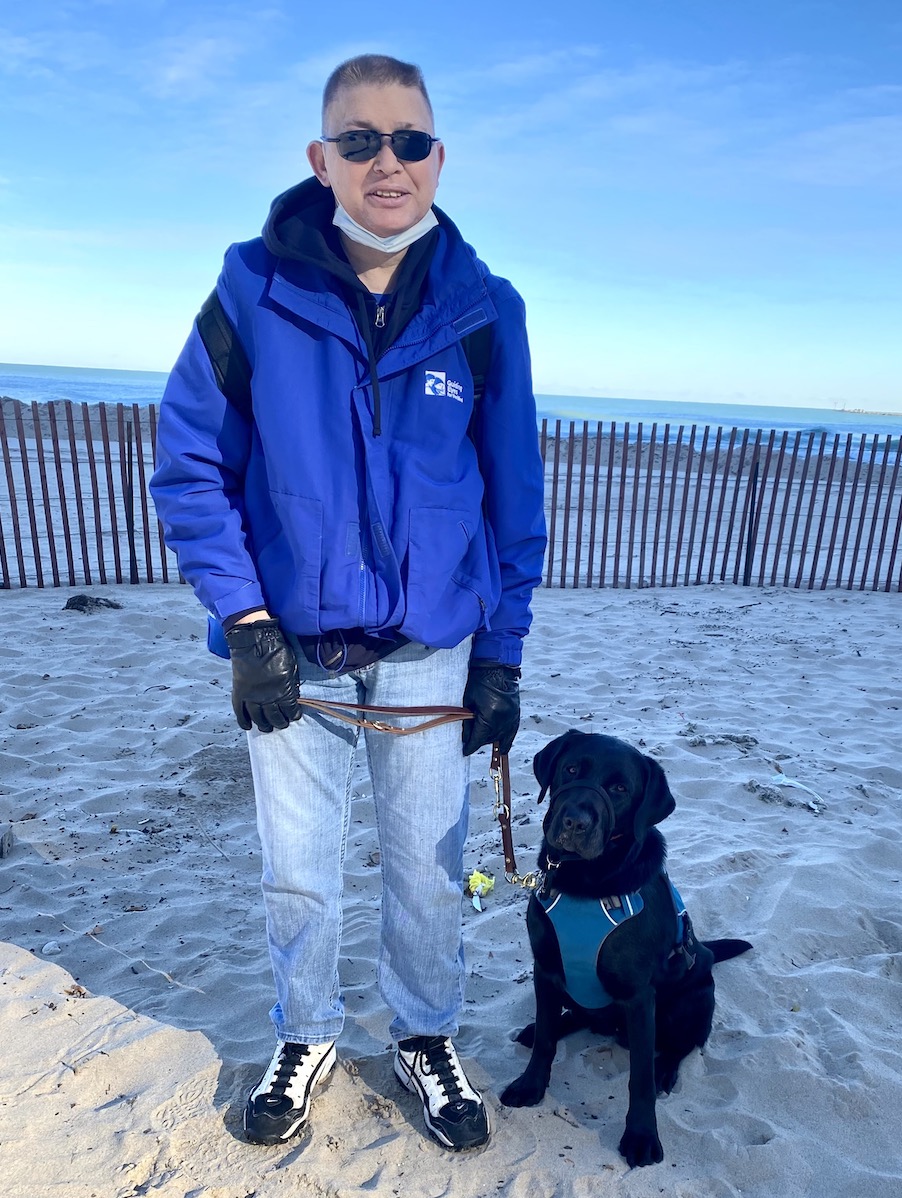 Grad Chris and guide Coda stand in the sandy of shore of Lake Michigan