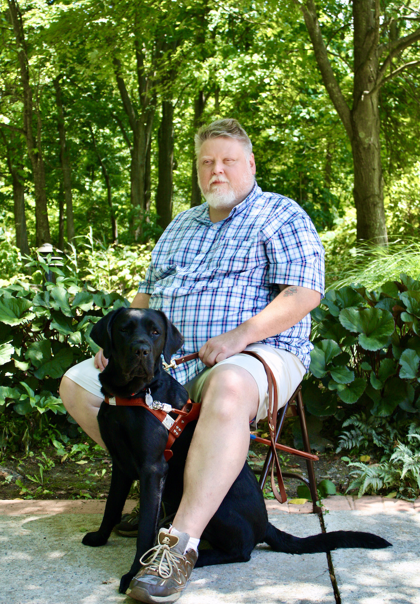 Graduate Christopher sits with his guide dog Jenko
