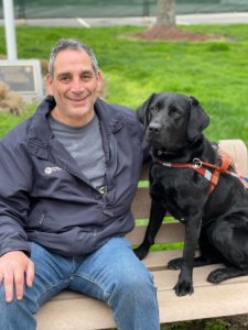 Graduate David and guide dog Claudette share an outdoor bench