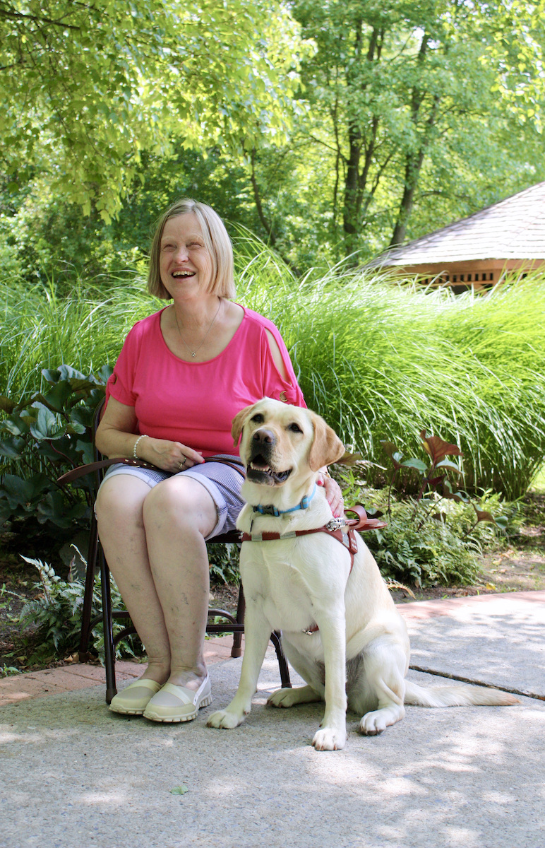 Graduate Dawn sits in a shady spot with smiling guide dog Meadow