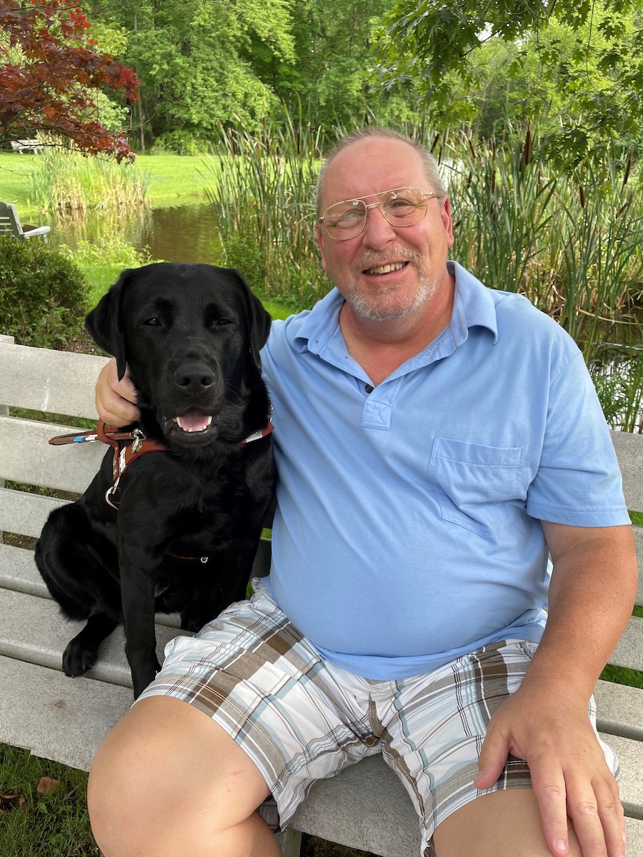 Graduate Donald sits on a bench with guide dog Rose