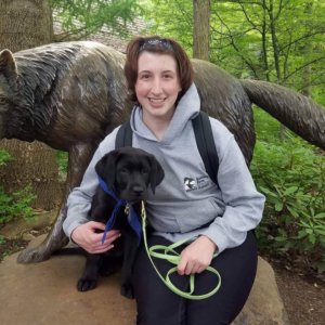 Julia sits on the base of a wolf statue with black lab puppy Dakota sitting next to her.