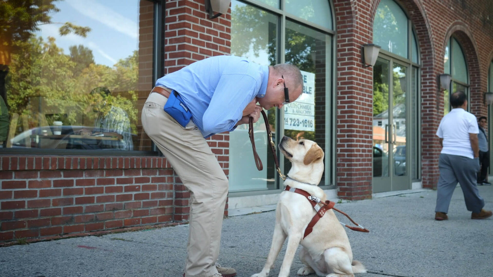 David bends down to share a moment with guide dog Tessi, a yellow lab in harness.