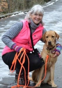Jana kneels with her arm around yellow lab Blue who sits on the icy path.