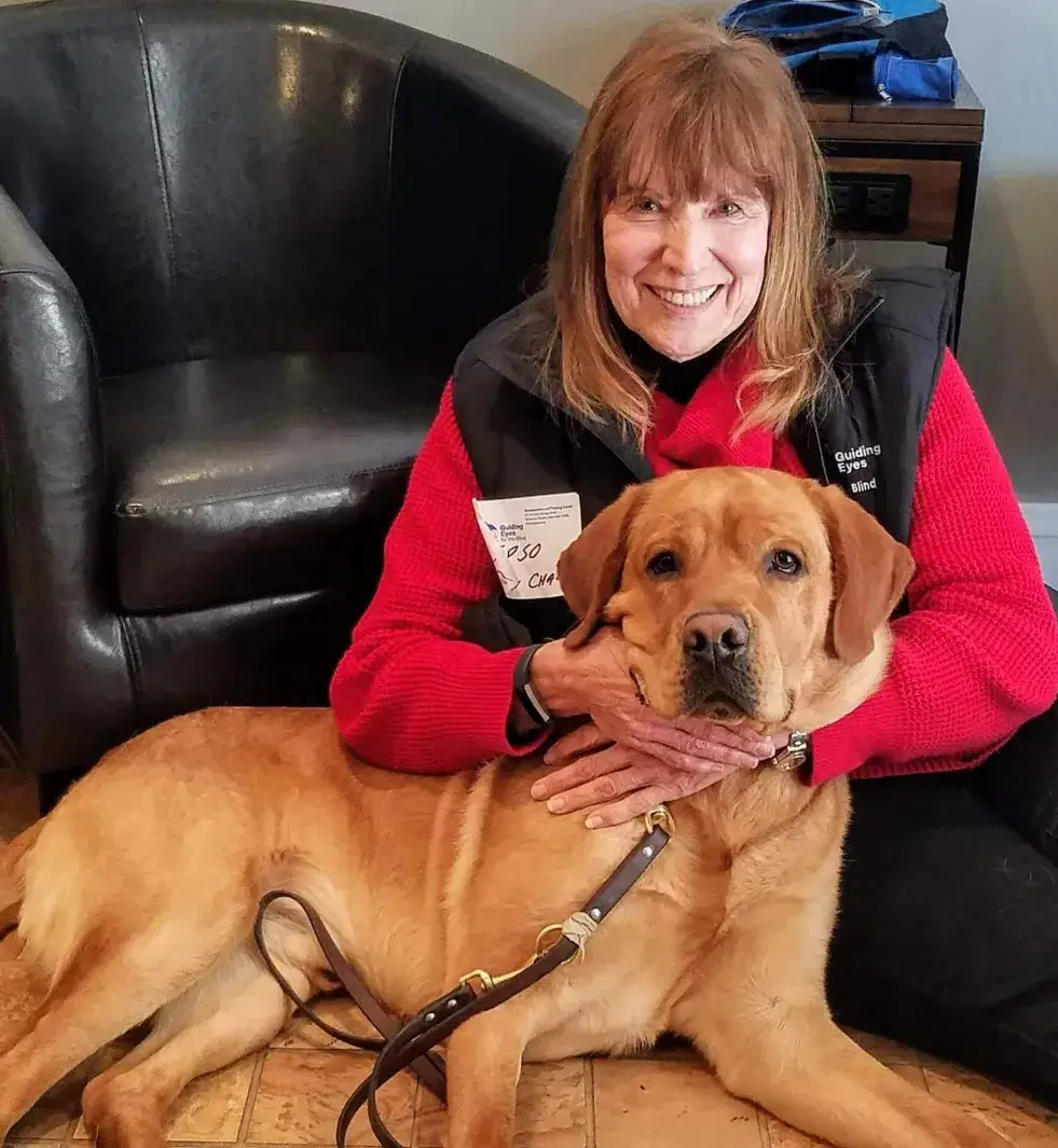 Susan sits on the floor and holds ipso's head in her hands as she poses for a final photo with him before he enters harness training.