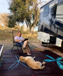 Woody sits in the camping chair outside the motorcoach with yellow lab Flyer napping on the rug at her feet.