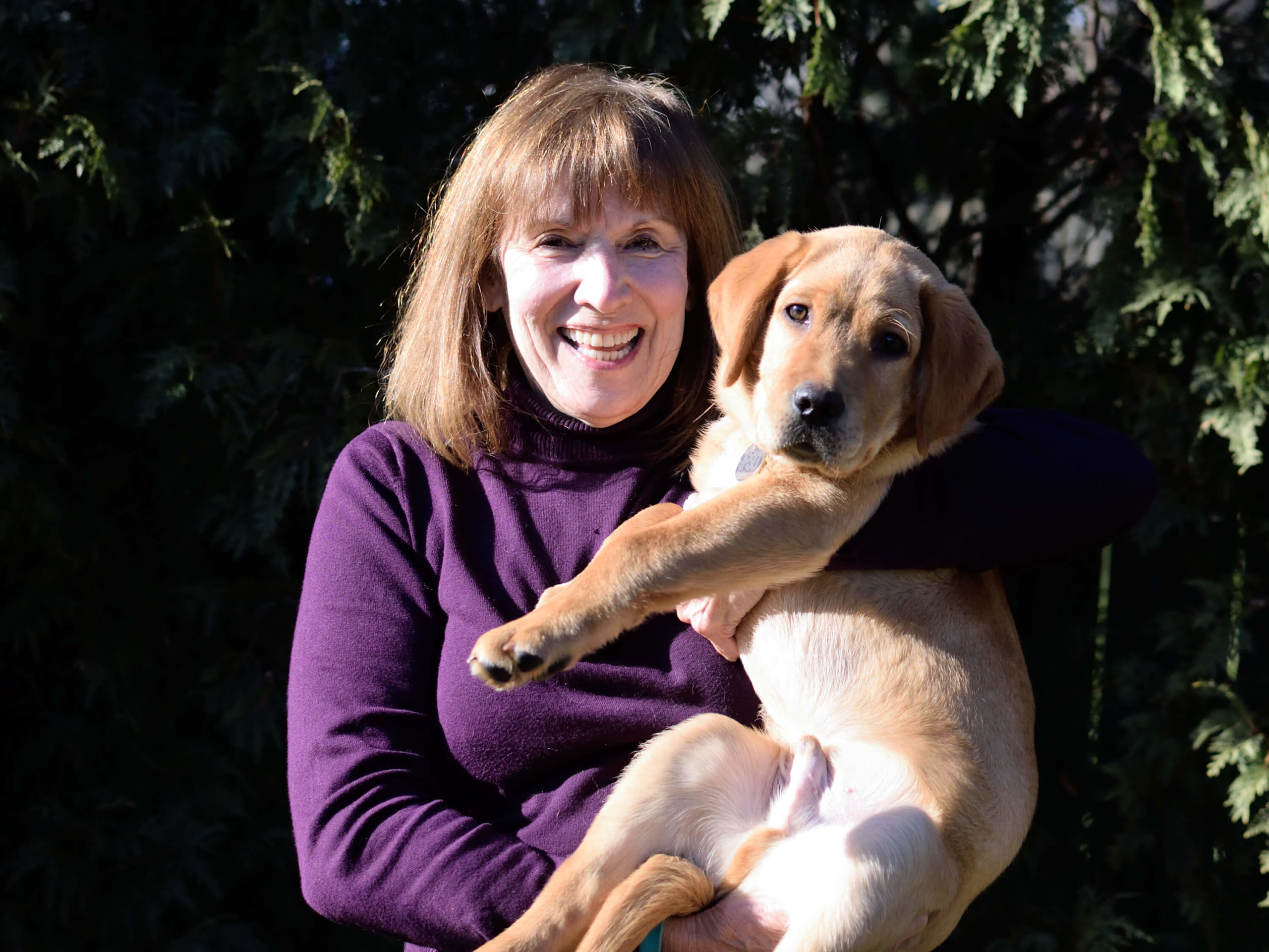 Susan holds fox red lab puppy Ipso in her arms and smiles for the camera.
