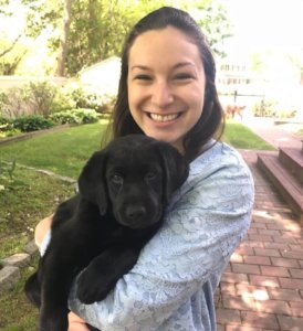 Jamie smiles for the camera while holding black lab puppy Secret in her arms.