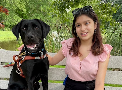 Graduate Joicee sits on a bench beside black Lab guide dog Junie