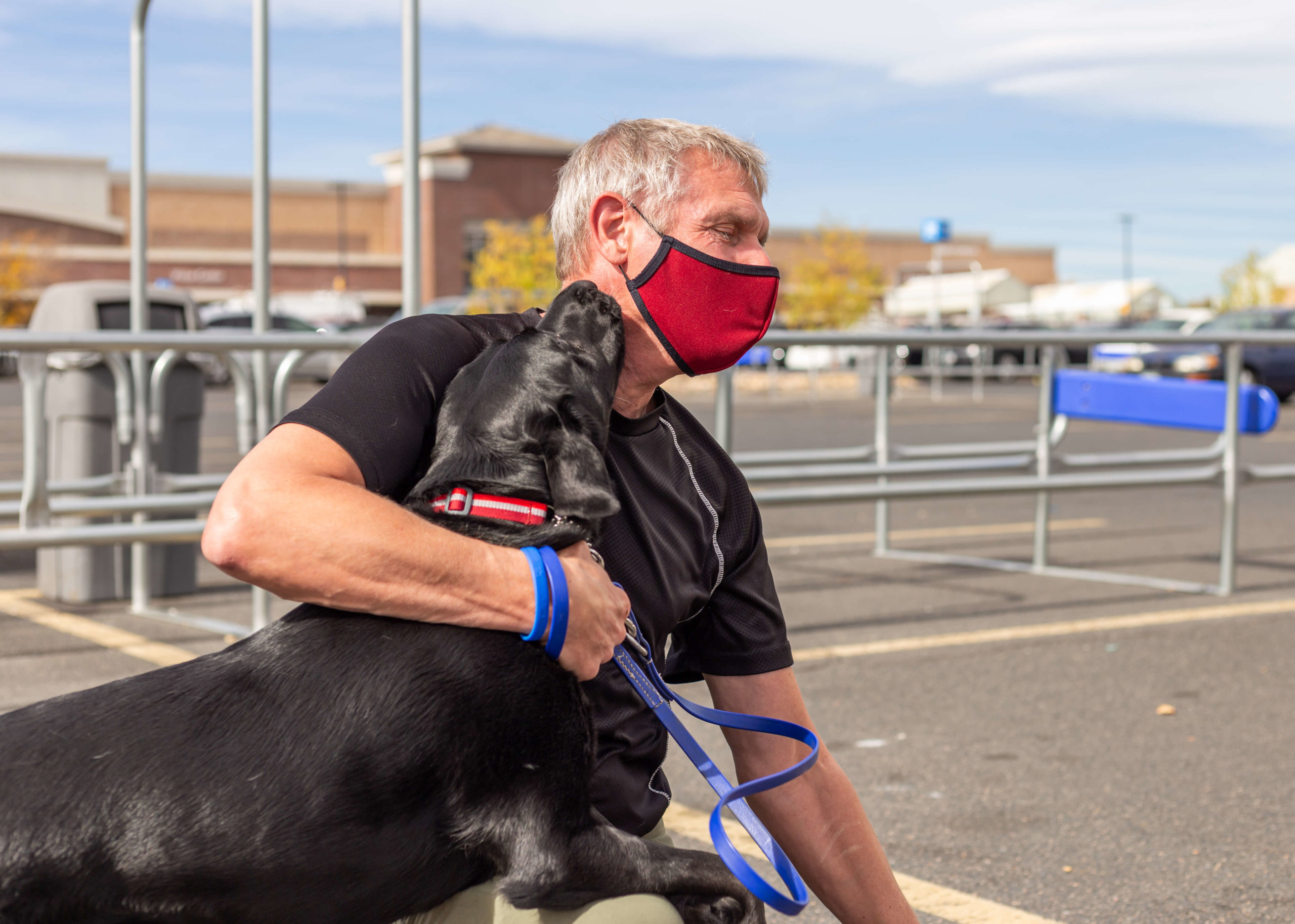A black lab gives a hello kiss to their foster volunteer who wears a face mask.