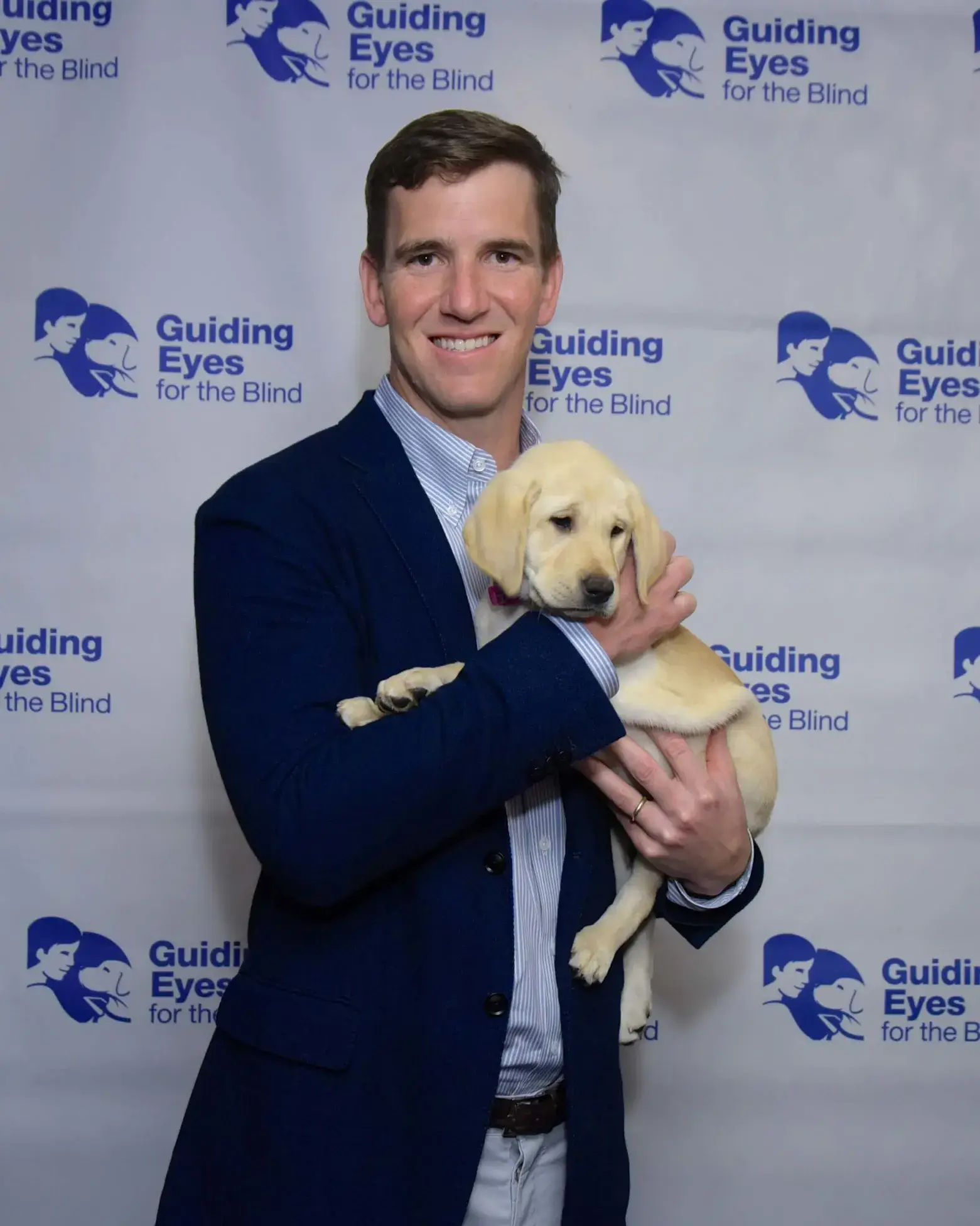 Eli Manning stands in front of a step and repeat at a Guiding Eyes event
