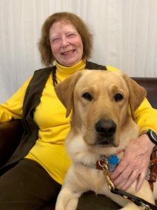 Graduate Kathy and guide dog Valance sit on a sofa and smile for a photo together