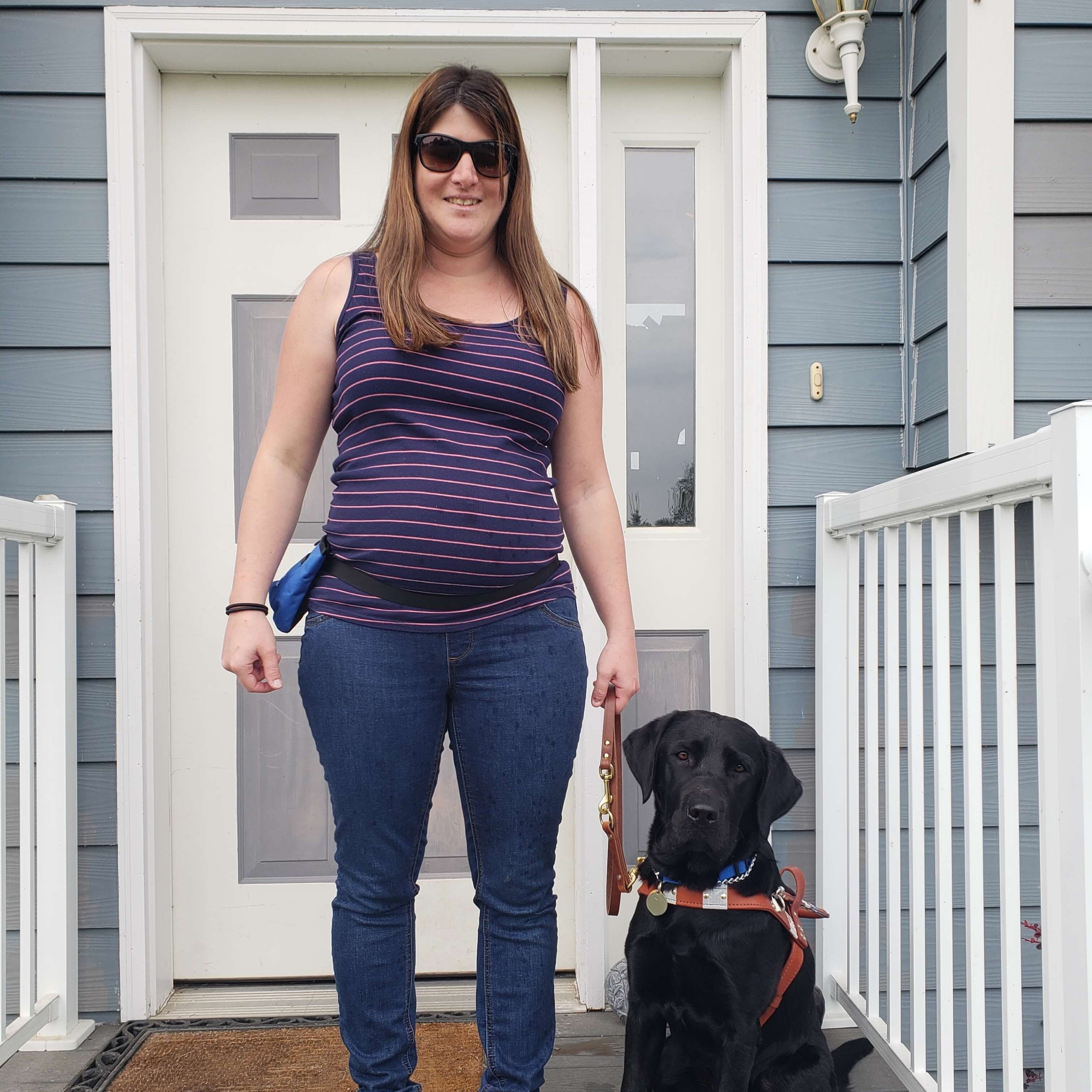 Graduate Kayla and guide dog Julie stand outside on a porch and smile for a photo