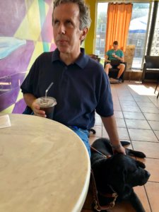 2018 graduate Matthew sits at his favorite coffee shop with guide dog Scout by his side