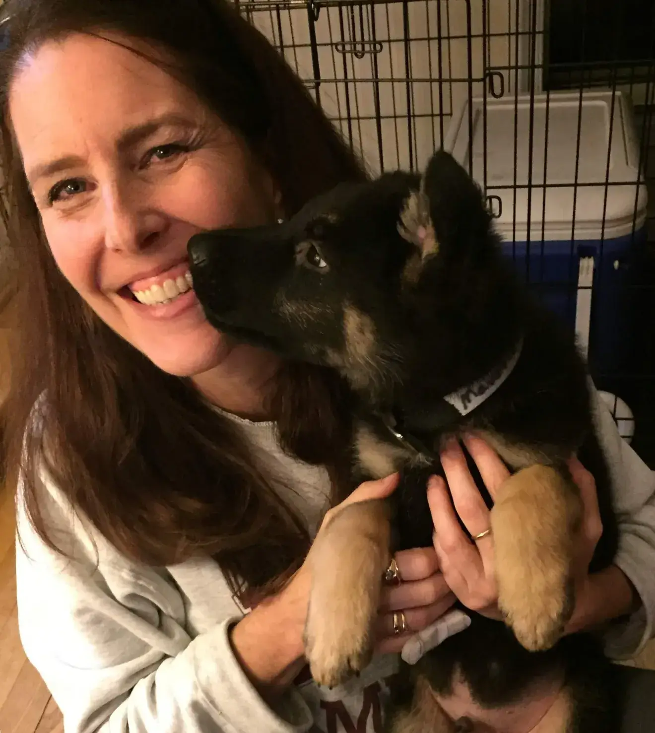Amy smiles while holding black and tan German shepherd puppy Maverick in her arms. Maverick turns his head to give Amy a kiss on her face.