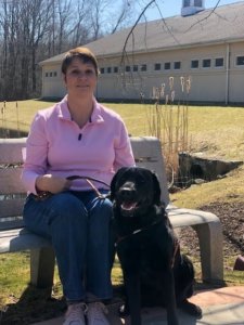 Graduate Michelle and guide dog Farrow sit on a bench in the warmth of the spring sunshine