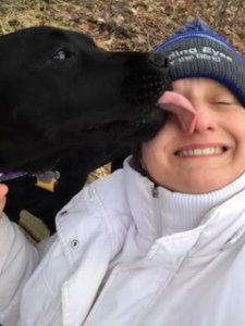 Danielle closes her eyes and smiles for a selfie with black lab Nestle. Nestle gives Danielle a kiss on the face as the picture is taken.