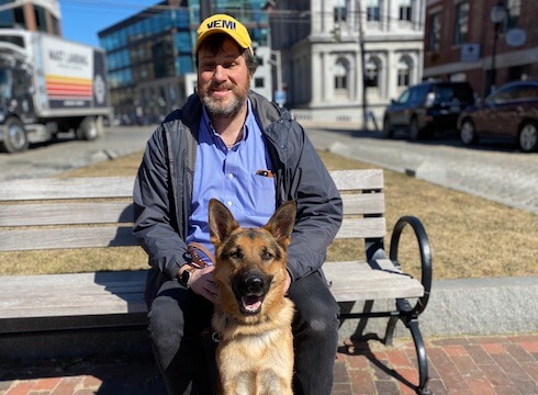Nicholas and guide dog Norbert sit on a sunny bench
