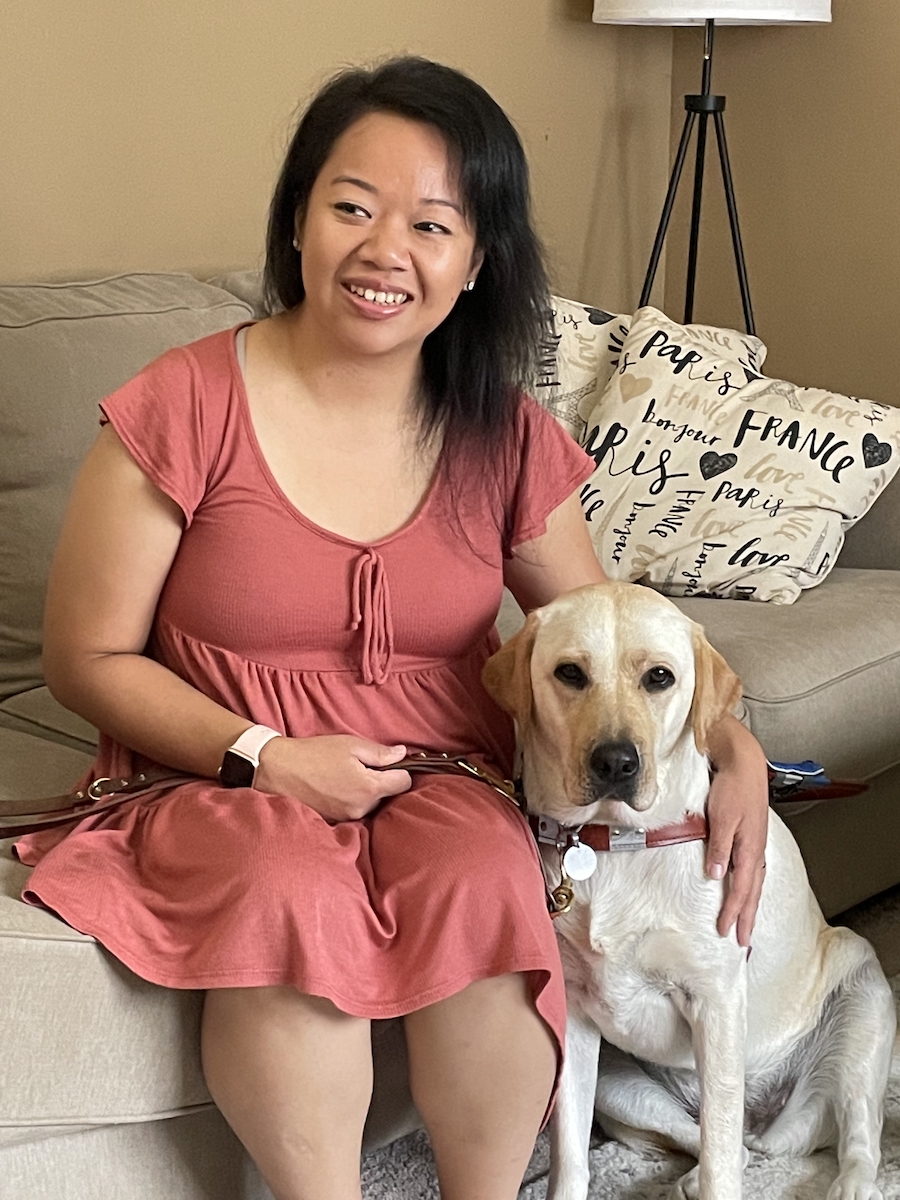 Grad PangNhia in a rose colored dress sits next to guide dog Elana