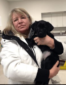 Peggy holds an adorable black lab puppy while visiting the Canine Development Center campus.