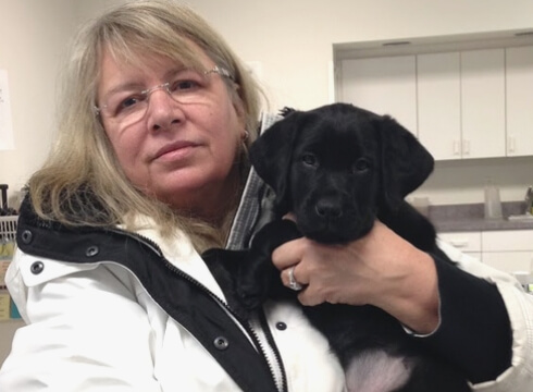 Peggy holds an adorable black lab puppy while visiting the Canine Development Center campus.