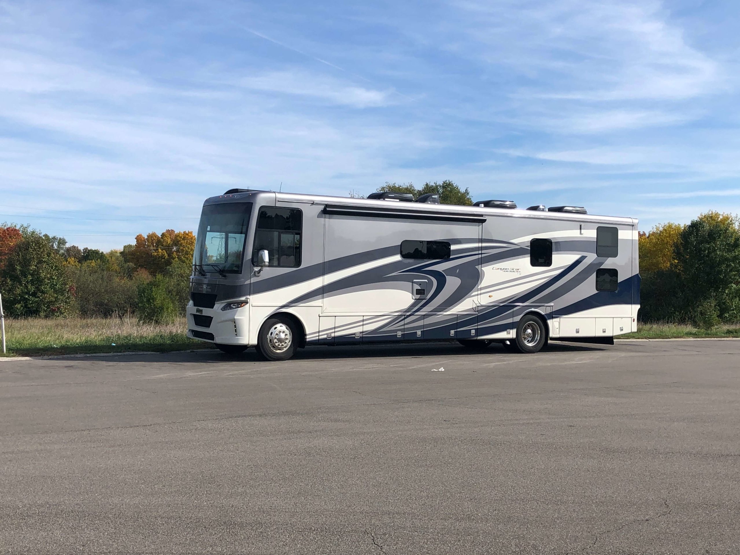 The grey and off-white motor coach sits in a empty parking lot during a quick rest stop break. 