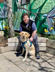 Graduate Sadie and guide dog Legend sit among the tulips and a bright painted wall