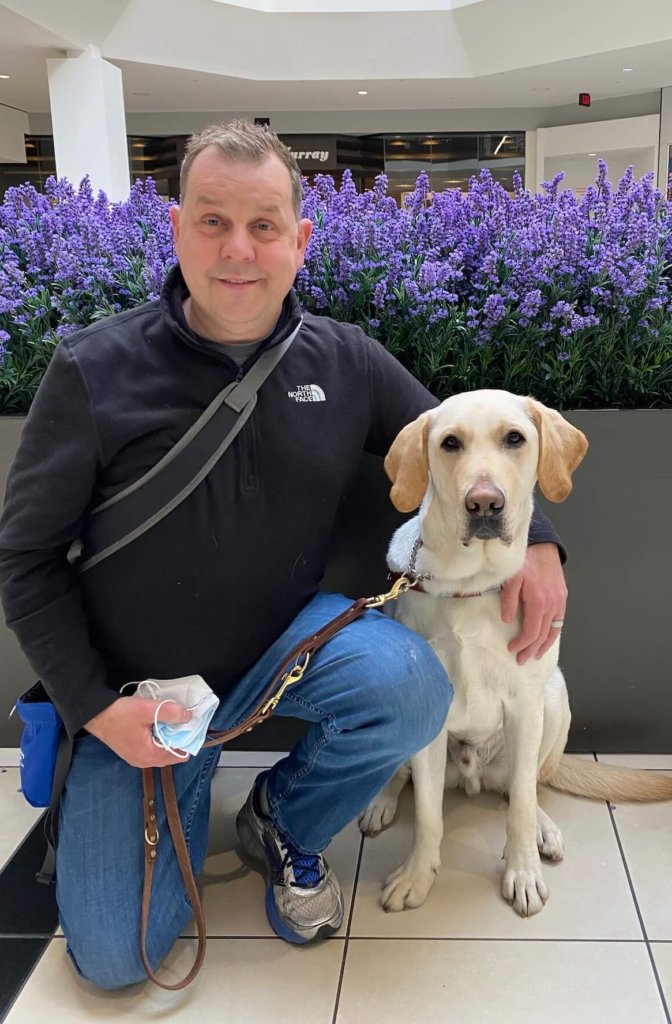 Samuel kneels next to his guide dog Stan while training at the mall