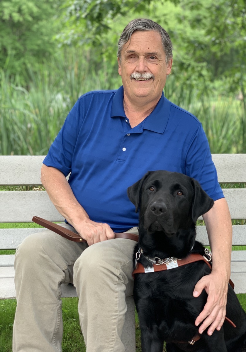 Graduate Terry sits on a bench with his new companion and guide dog Namath at his side