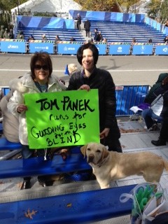 Linda Press, Melissa Panek and Gus await Tom with a sign that says "Tom Panek runs for Guiding Eyes for the Blind!"