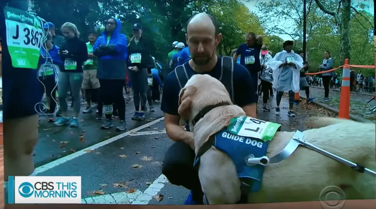 President & CEO Thomas Panel kneels down next to his guide dog Gus before running a race