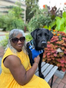 Graduate Barbara sits on a bench with black Lab guide dog Quasar
