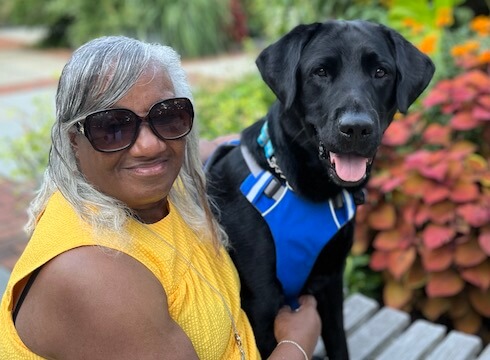Graduate Barbara sits on a bench with black Lab guide dog Quasar
