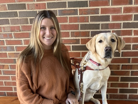 Graduate Carly and yellow Lab guide dog Sharon sit on a bench against a brick wall