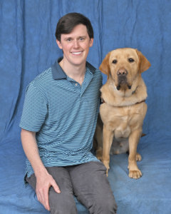 Alexander and yellow Lab guide dog Ballou pose against blue background