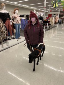 Amanda and black Lab guide Brava walk through clothing aisles at the mall