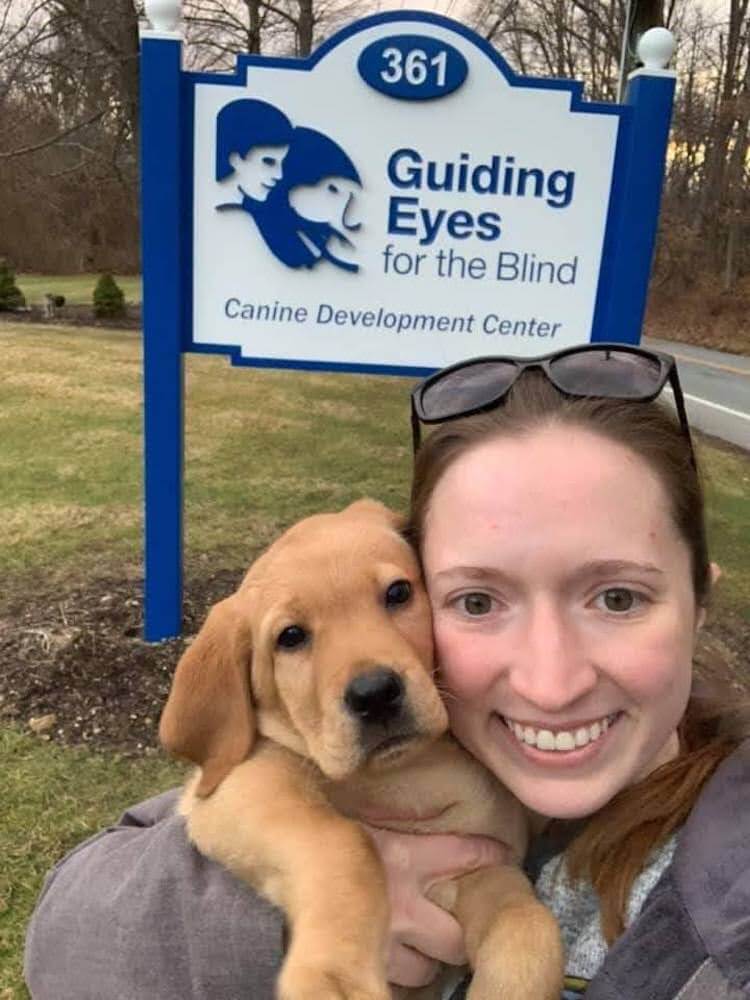 Raiser Kyle snuggles puppy Yani at the CDC's Guiding Eyes sign