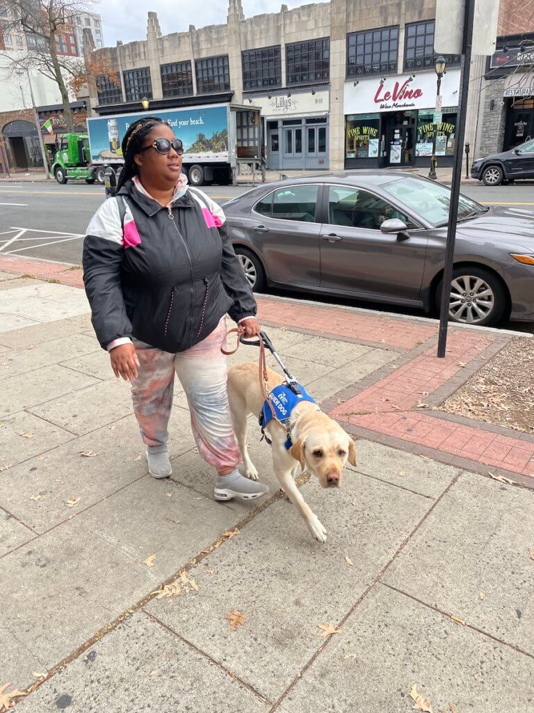 Briasa walks with guide dog Journey along a wide sidewalk
