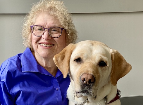 Gail sits next to yellow Lab guide dog Journey for their team portrait